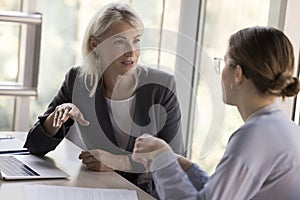 Two young and mature business colleagues women talking at table