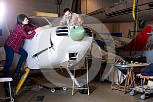 Two young mechanics, man and woman, repairing light sport plane in workshop