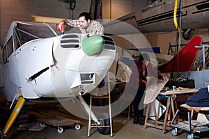 Two young mechanics, man and woman, repairing light sport plane in workshop