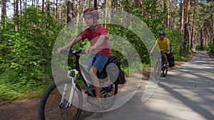 Two young men with backpacks ride bicycles along the road.