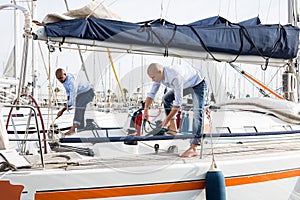 Two young men in blue shirts tidy up private sailing yacht in the seaport