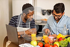 Two men using laptop in kitchen