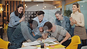 Two young men competing arm wrestling in office. Joyful colleagues clapping hands, laughing and having fun.