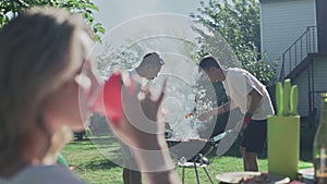 Two young men cooks on bbq grill. Blured woman on foreground