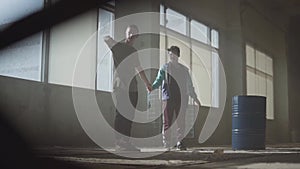 Two young men dancing in the dark and dusty room of abandoned building. Teenagers making dance move simultaneously