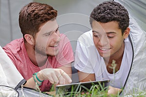 Two young men layed in tent looking at tablet