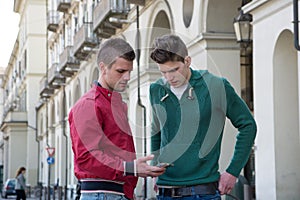 Two Young Men Looking Down at Cell Phone Outdoors