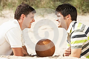 Two Young Men Relaxing On Beach With Football