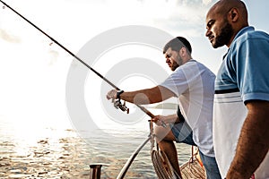 Two young men standing on sailboat with fishing rod looking at haul
