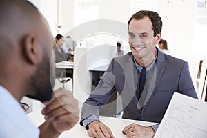 Two young men talking at a meeting in an open plan office