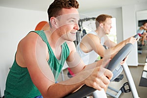 Two Young Men Training In Gym On Cycling Machines Together