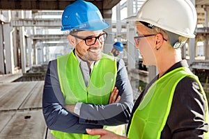 Two young modern architects or civil engineers talking about future project development on a construction site photo