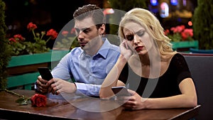 Two young people boring on date, using smartphones, problems in relationship