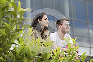 The two young people, a boy and a girl, standing, leaning against the fence and see the area