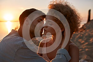 Two young people in love, couple looking passionate, kissing each other on the beach at sunset