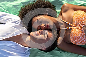 Two young people lying down cheek to cheek on a beach towel with eyes closed