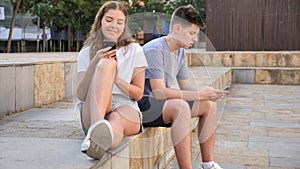 Two young people with mobile phones are sitting on the step