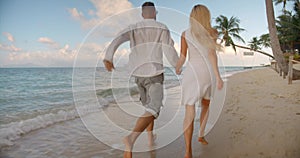 Two young people running along the sandy ocean beach hand in hand enjoying tropical evening warmness