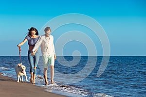 Two young people running on the beach kissing and holding tight with dog