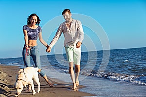 Two young people running on the beach kissing and holding tight with dog