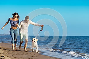 Two young people running on the beach kissing and holding tight with dog