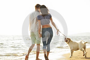 Two young people running on the beach kissing and holding tight with dog