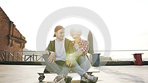 Two young people are sitting on the skateboard on the roof of the industrial building. Young couple have fun sits on the