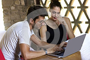 Two young people sitting on a wooden table looking at laptop