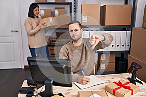 Two young people working at small business ecommerce with angry face, negative sign showing dislike with thumbs down, rejection
