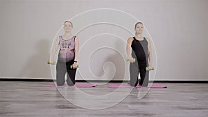 Two young pregnant women do fitness gymnastics in a sports club