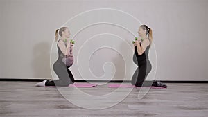 Two young pregnant women do fitness gymnastics in a sports club