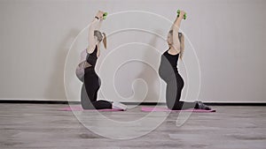 Two young pregnant women do fitness gymnastics in a sports club