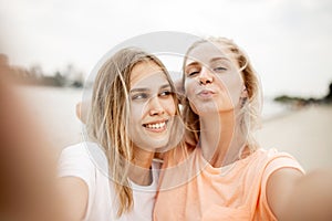 Two young pretty blonde girls take a selfie on the beach on a warm windy day