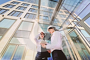 Two young pretty business women industrial engineers in construction helmets with a tablet in hands on a glass building