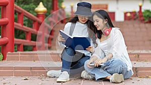 Two young pretty female teenagers starring idea while reading together on staircase in university