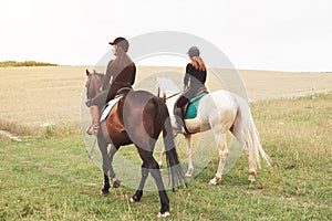 Two young pretty girls riding a horses on a field. They loves animals andhorseback riding
