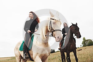 Two young pretty girls riding a horses on a field. They loves animals andhorseback riding