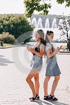 Two young pretty girls on a walk in the park with phones. sunny summer day, joy and friendships