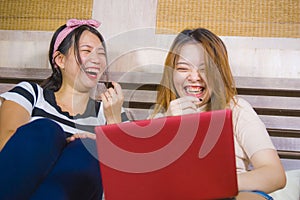 Two young pretty and happy Asian Chinese student girls together at home bedroom using internet social media in laptop computer