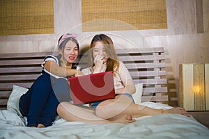 Two young pretty and happy Asian Korean student girls together at home bedroom using internet social media in laptop computer