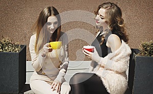 Two young pretty happy woman sitting outdoors and drinking coffee. Lifestyle concept of happy people.