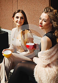 Two young pretty happy woman sitting outdoors and drinking coffee. Lifestyle concept of happy people.