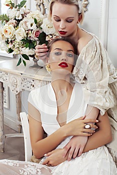 Two young pretty lady in white lace fashion style dress posing in rich interior of royal hotel room, luxury lifestyle