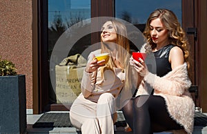 Two young pretty woman laughing outdoors and drinking coffee. Li