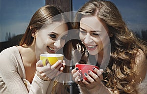 Two young pretty woman laughing outdoors and drinking coffee. Li