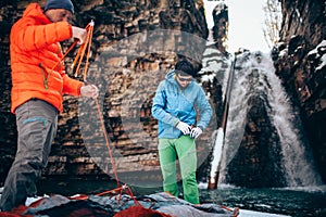 Two young professional male tourists are preparing to camp in the mountains near the river in winter.