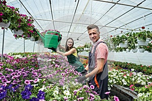 Two young satisfied people watering plants in beautiful garden center