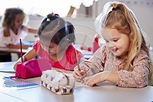 Two young schoolgirls sitting at a desk in an infant school classroom working, close up photo