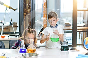 Two young scientists in protective glasses doing intereting chemical experiments with colored liquids and dry ice in