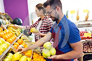 Two young sellers selecting fresh fruit and preparing for working day in fruitshop.